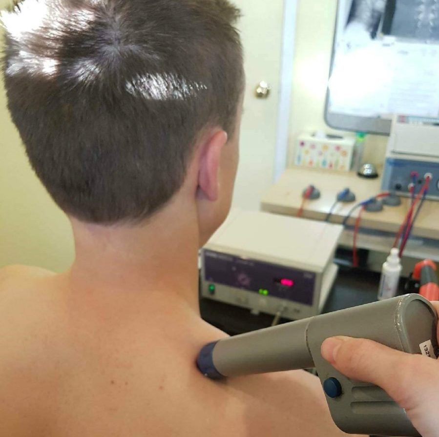 a shockwave gun being used on a shirtless male patient oakville
