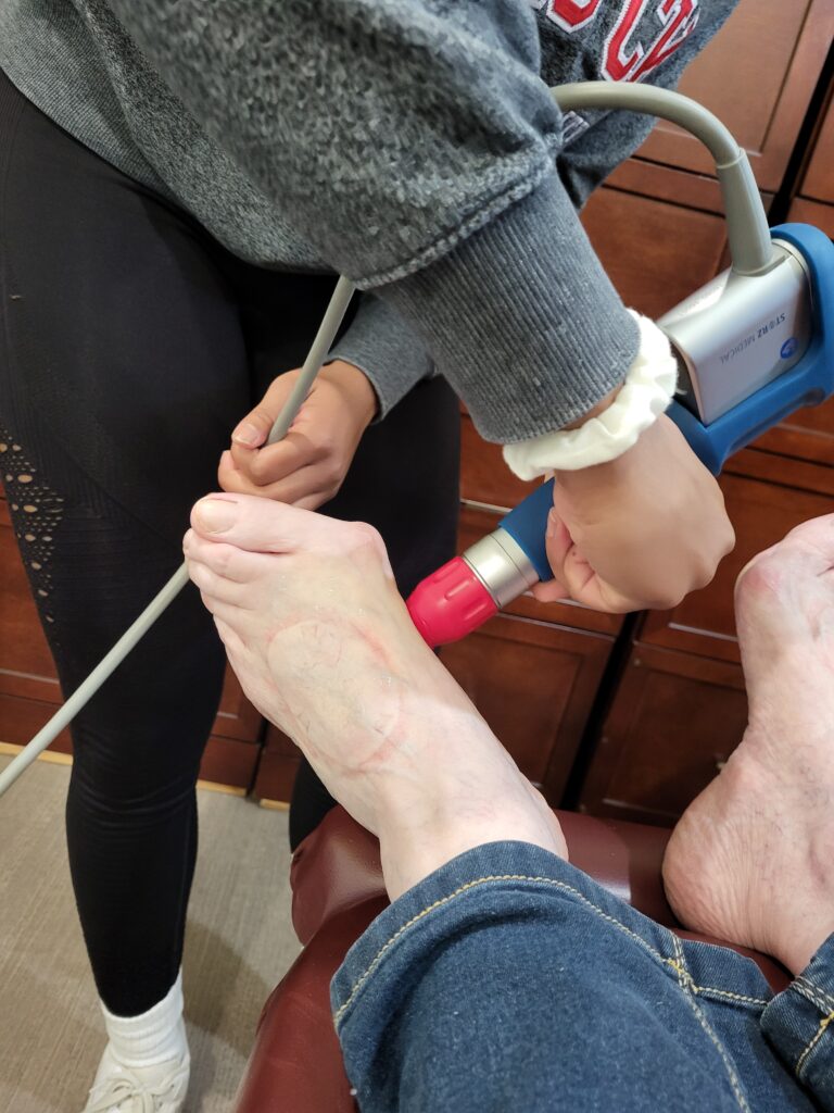 Shockwave therapy being used on a patients bunion, Silver gun with a red applicator head on inside of big toe.