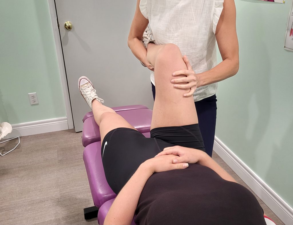 female patient lying on her back with physiotherapist working on her knee, looks like deep stretch of knee and front of leg