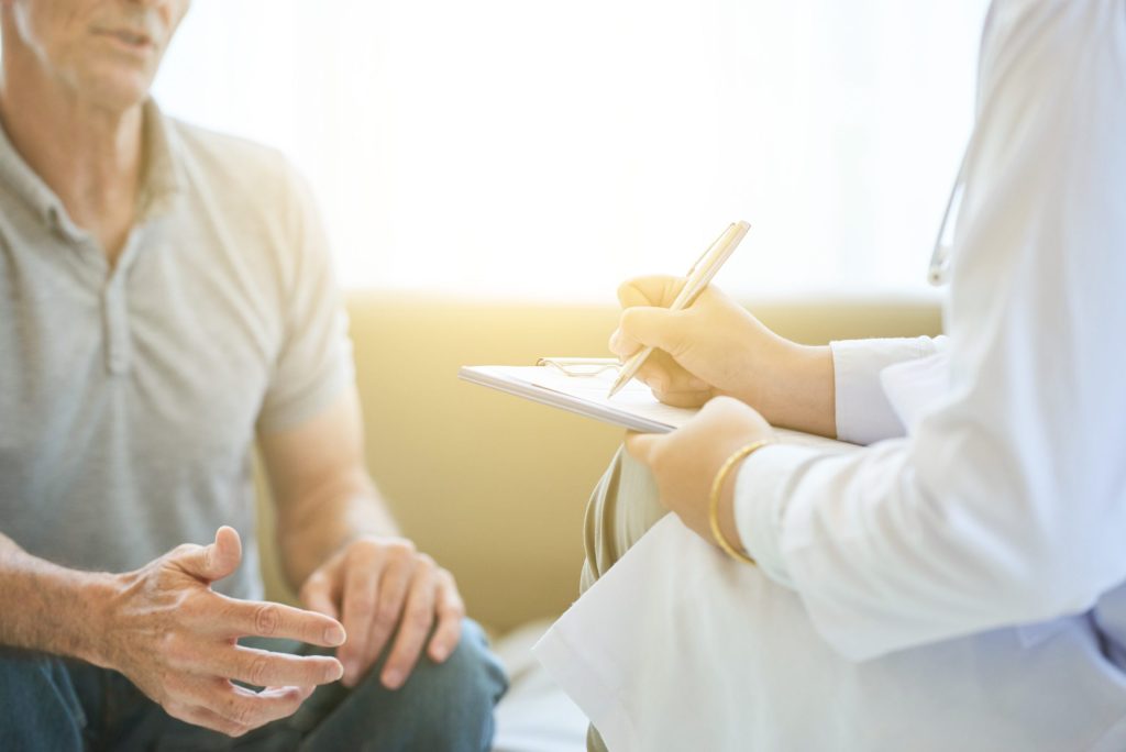 Doctor writing notes while speaking with a patient during a consultation.