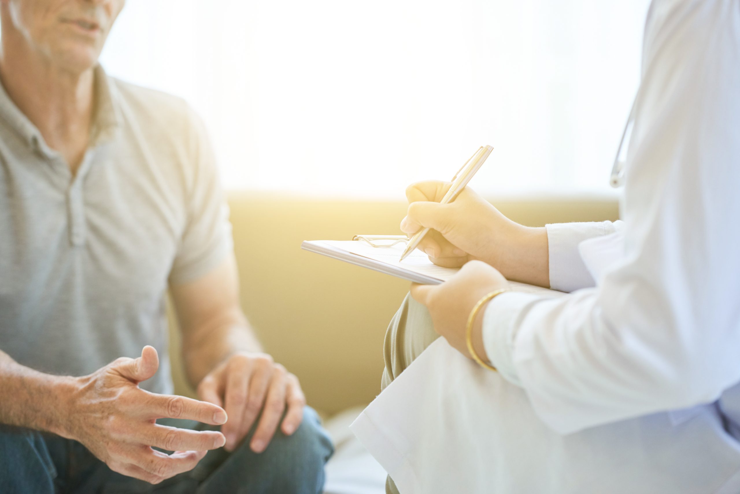 Doctor writing notes while speaking with a patient during a consultation.