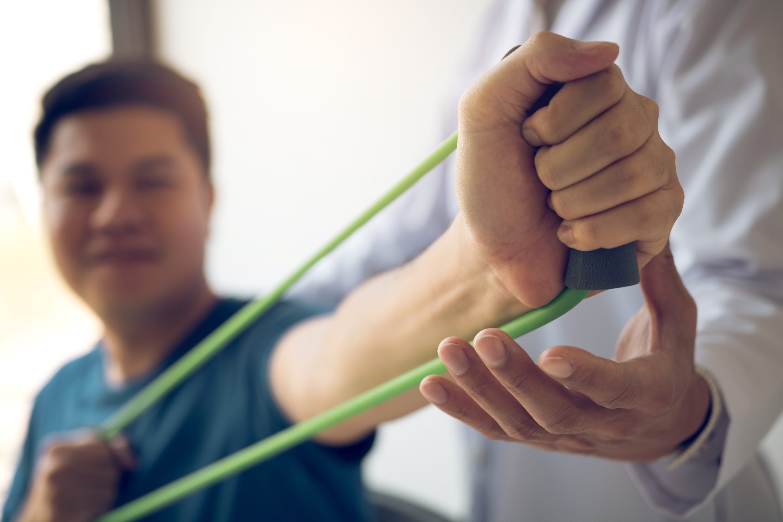 Therapist guiding a patient through resistance band shoulder exercise.