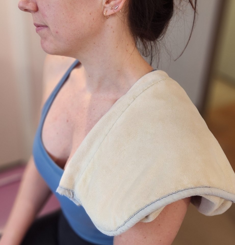 a female patient sitting in a treating room with a moist heat pack on her left shoulder