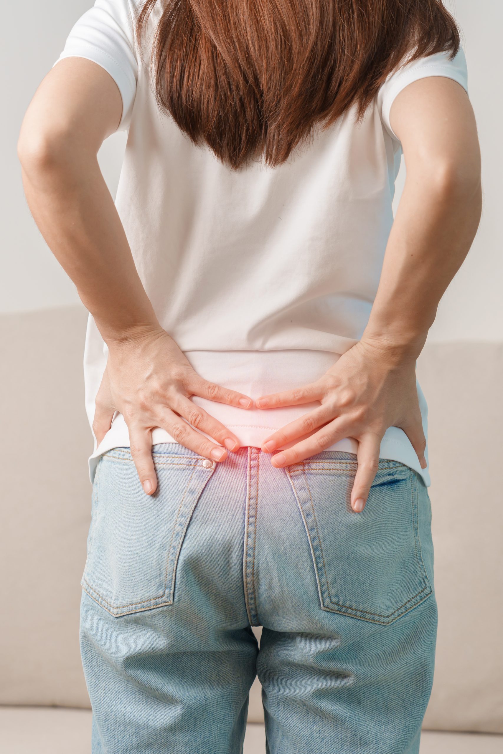 A lady holding her lower back with both hands near a red highlight to indicate pain or discomfort.