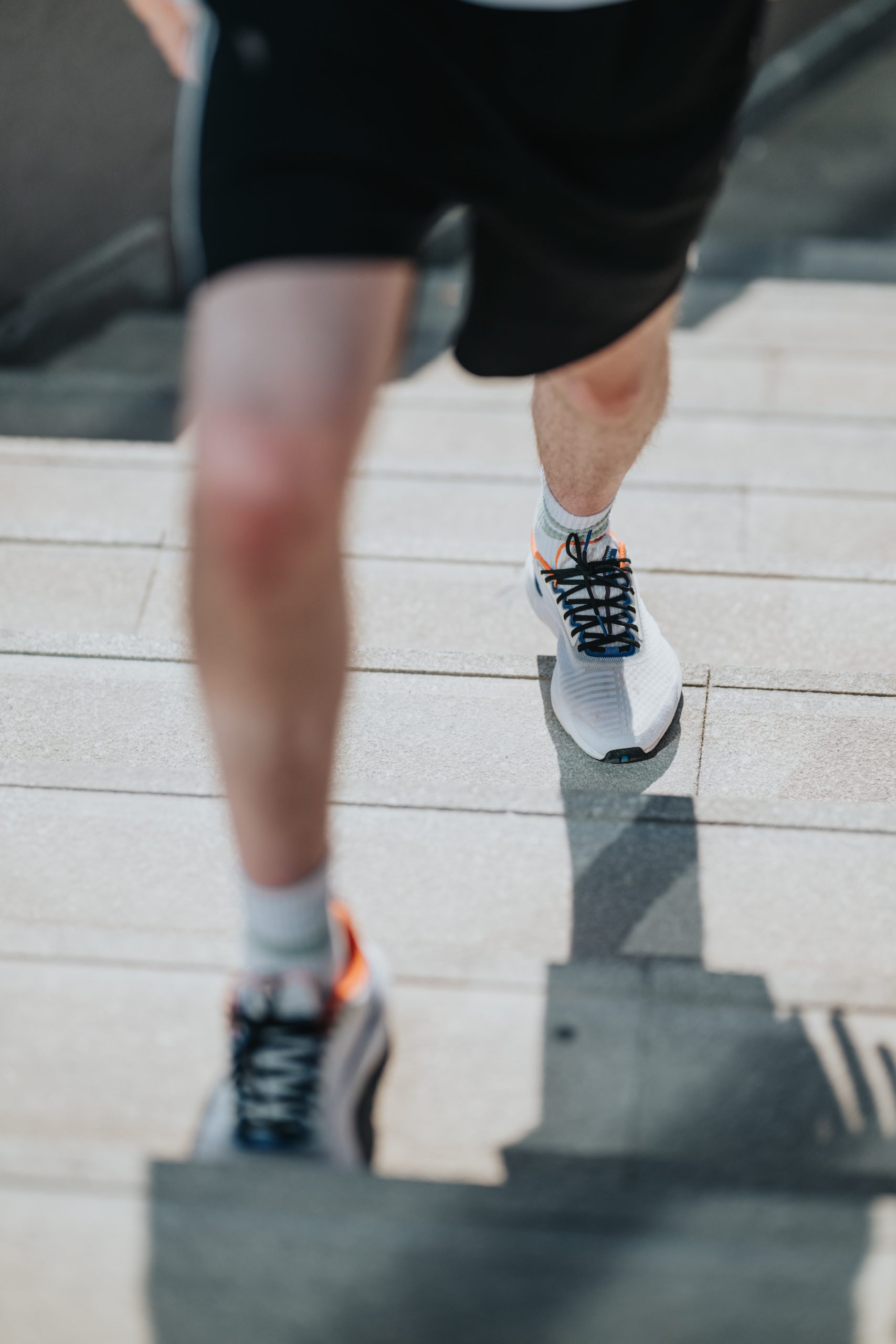 Close-up of a runner wearing athletic shoes while climbing outdoor concrete steps.