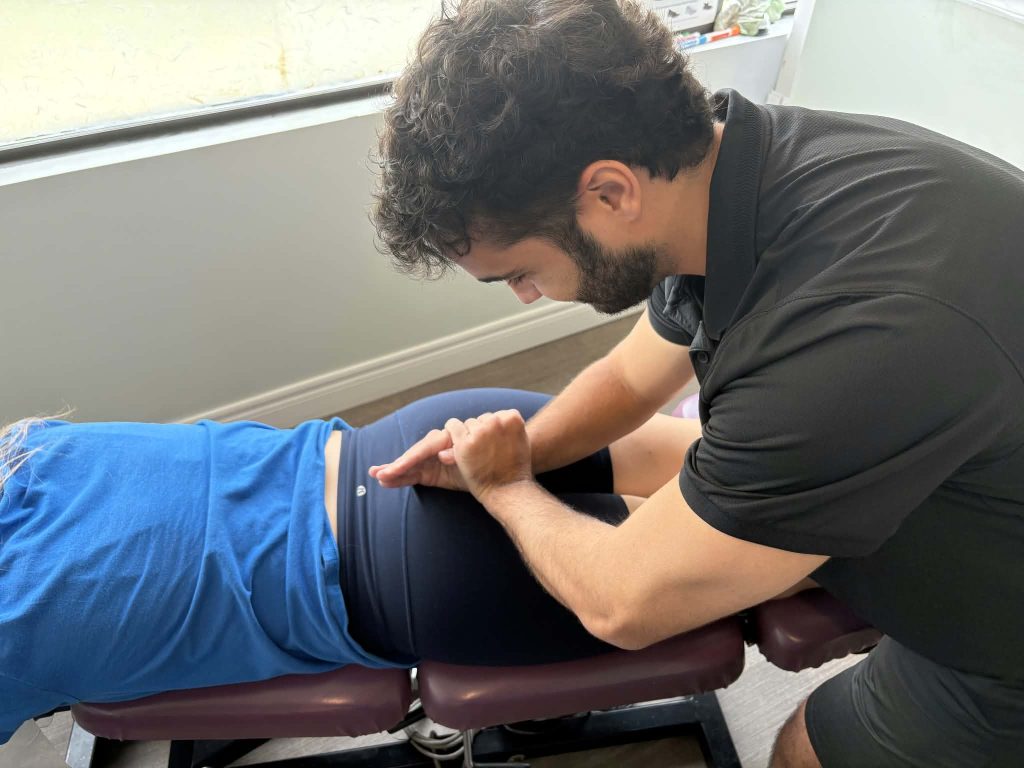 Dr. Alex performing a glute and tailbone adjustment with the female patient facedown
