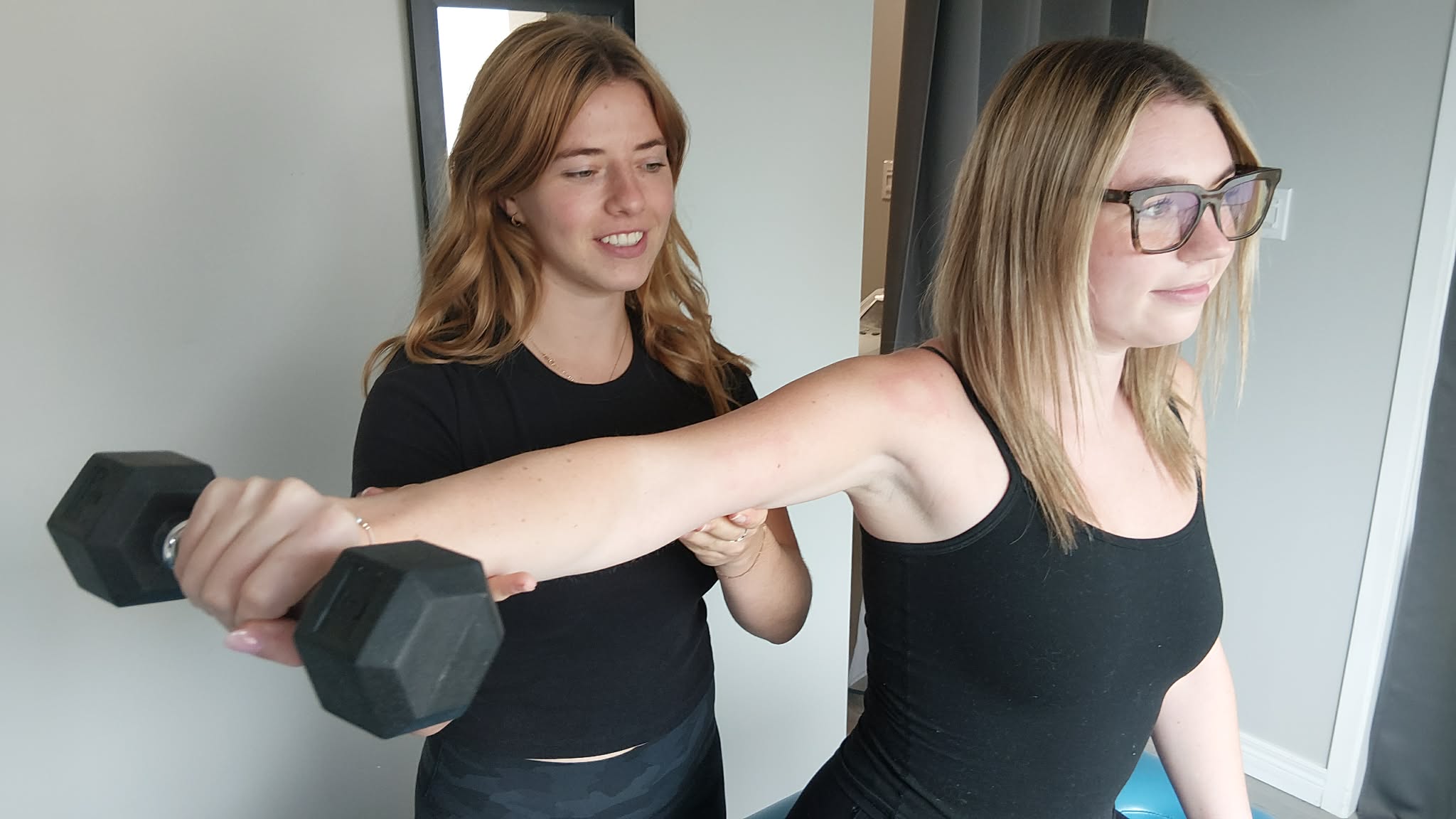 a female patient lifting a dumbbell with her arm, while the female physiotherapist assists
