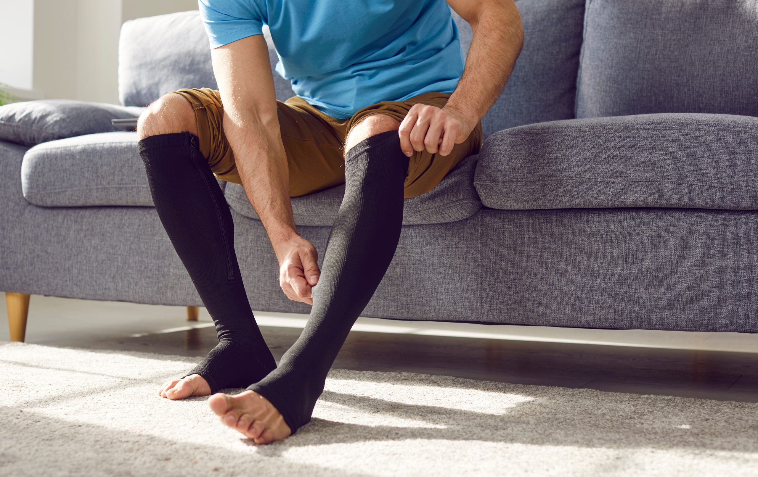 Man sitting on a sofa and adjusting black compression socks.